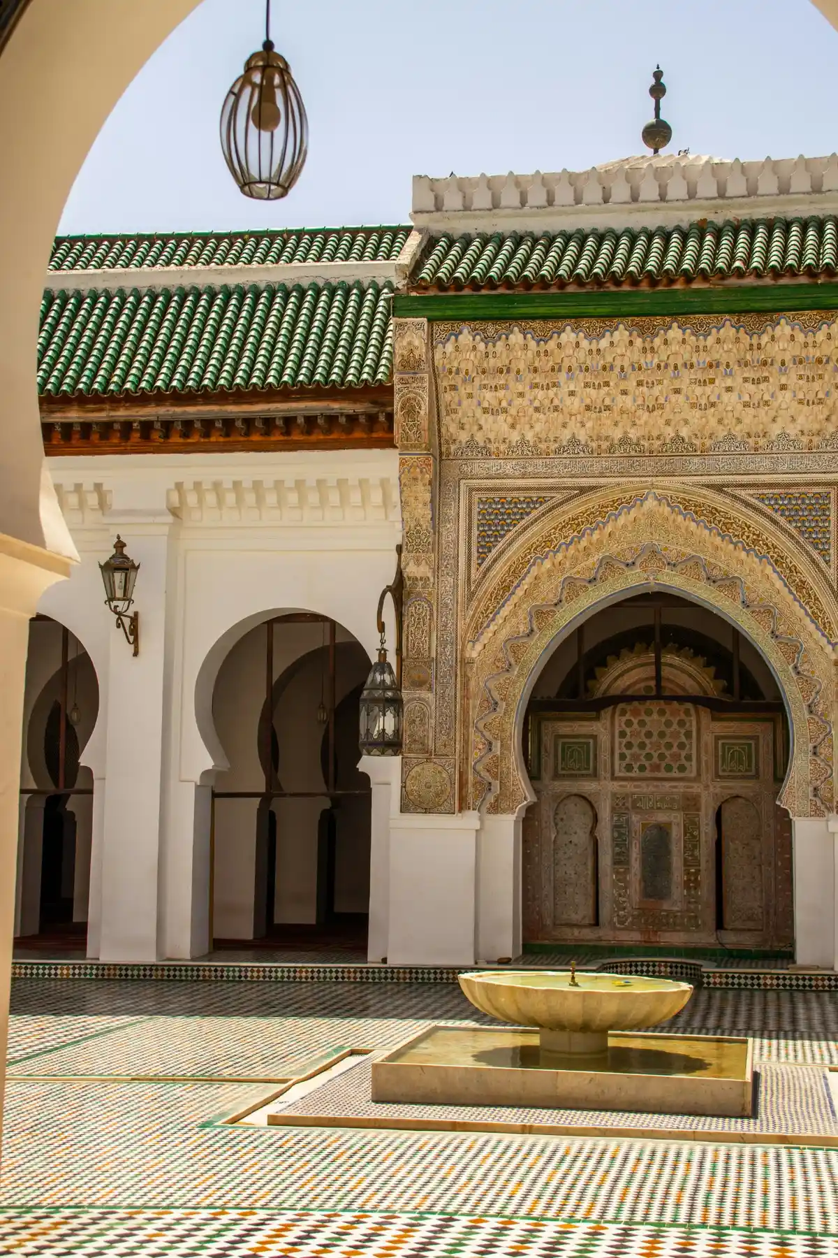 Intricate zellige tilework and carved plaster inside Al-Attarine Madrasa during guided Fez tours.